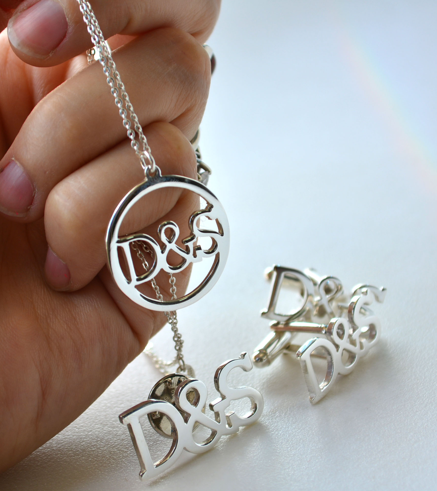 Joyería personalizada en plata con iniciales D&S, incluyendo mancuernillas y colgante circular, sobre fondo blanco
